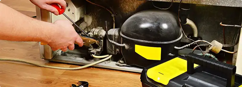 Refrigerator repair technician fixing the compressor and wiring in Crescent, IA