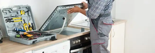 Cooktop repair technician lifting a built-in stovetop for service in Omaha, NE