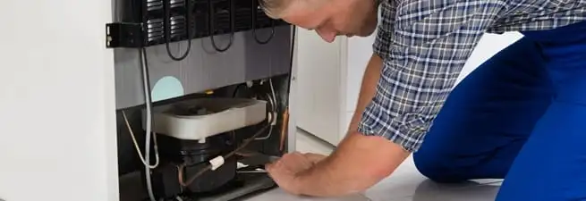Refrigerator repair technician servicing the compressor and condenser area in Omaha, NE