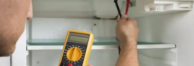 Refrigerator repair technician testing electrical components with a multimeter in Omaha, NE