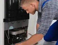 Refrigerator repair technician servicing the compressor and condenser area in Omaha, NE